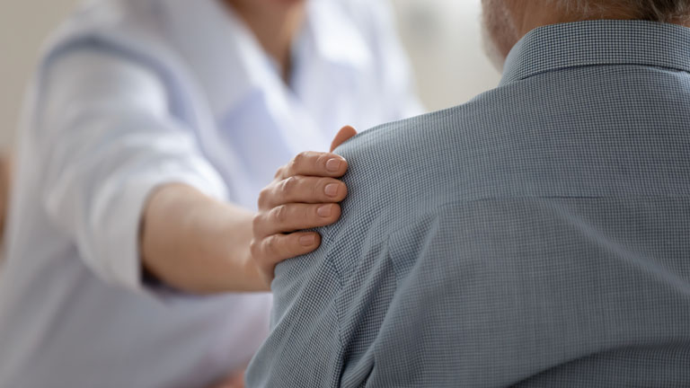Female interventional cardiologist reassures her patient with a hand on his shoulder