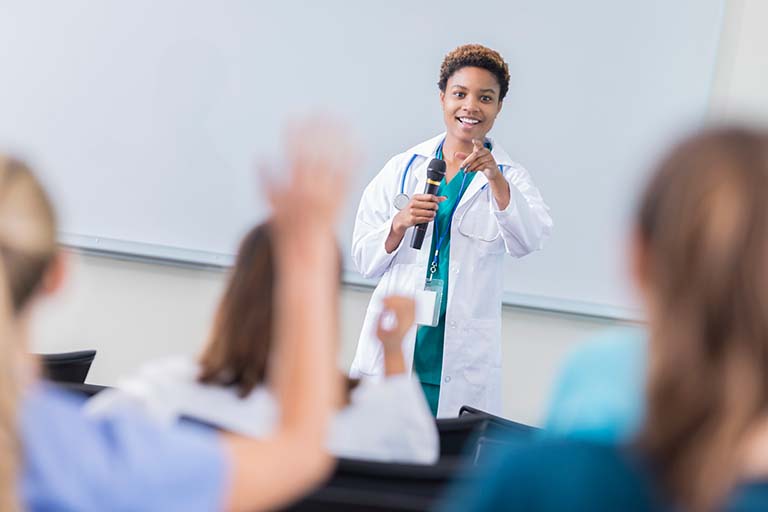 Female interventional cardiologist holding a microphone presenting to a room full of doctors